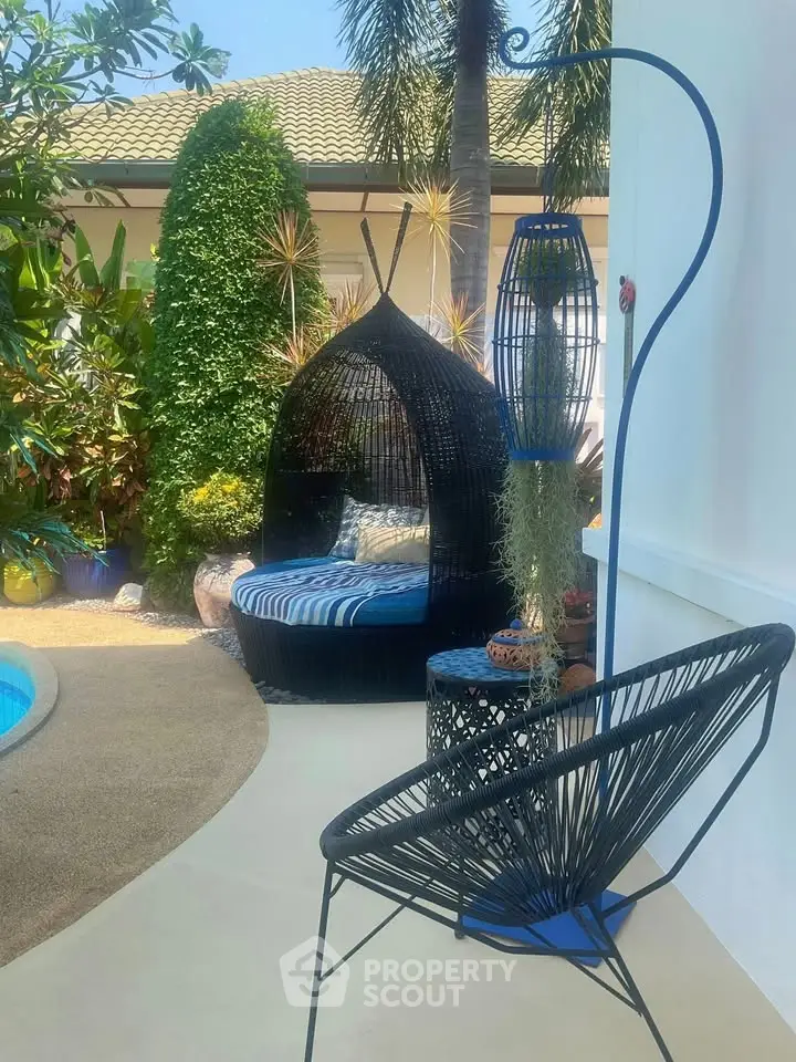 Charming outdoor seating area with stylish furniture by a pool, surrounded by lush greenery.