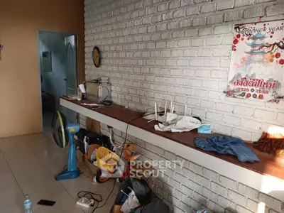 Cozy living room with white brick wall and wooden shelf, featuring eclectic decor and natural light.