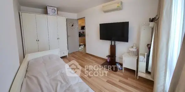 Cozy bedroom with wooden flooring, TV, and ample storage in a modern apartment.