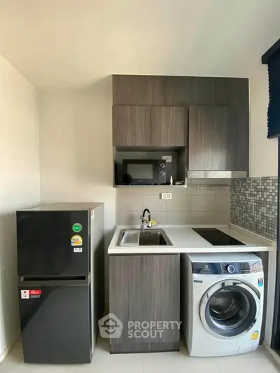 Modern kitchen with sleek cabinetry, washing machine, and fridge in compact layout.