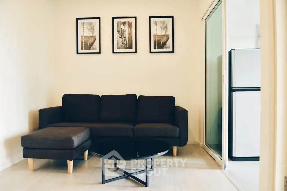 Modern living room with stylish black sofa and framed art, adjacent to a sleek kitchen area.