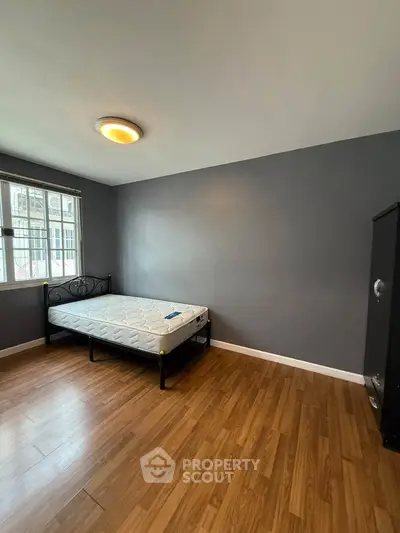 Spacious bedroom with wooden flooring and large window for natural light.