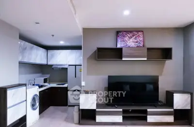 Modern living room with sleek entertainment center and adjacent kitchen featuring washing machine.