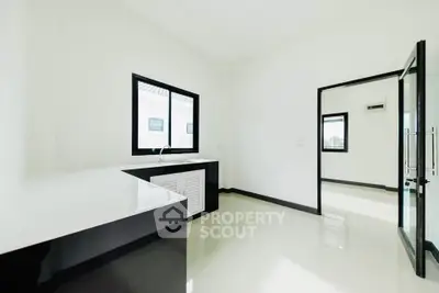 Modern minimalist kitchen with sleek black and white design, featuring large windows and ample counter space.