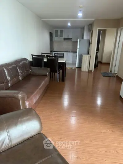 Spacious open-plan living room with modern kitchen and dining area, featuring sleek wooden flooring and leather sofas.