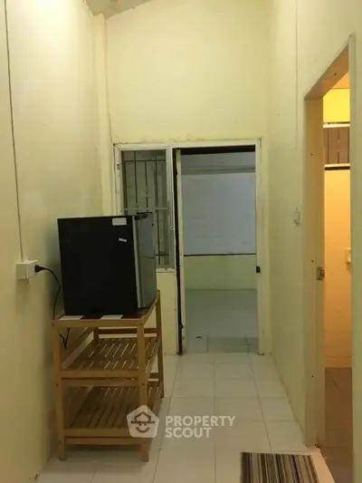 Compact hallway with small fridge and wooden shelf, leading to adjacent rooms.