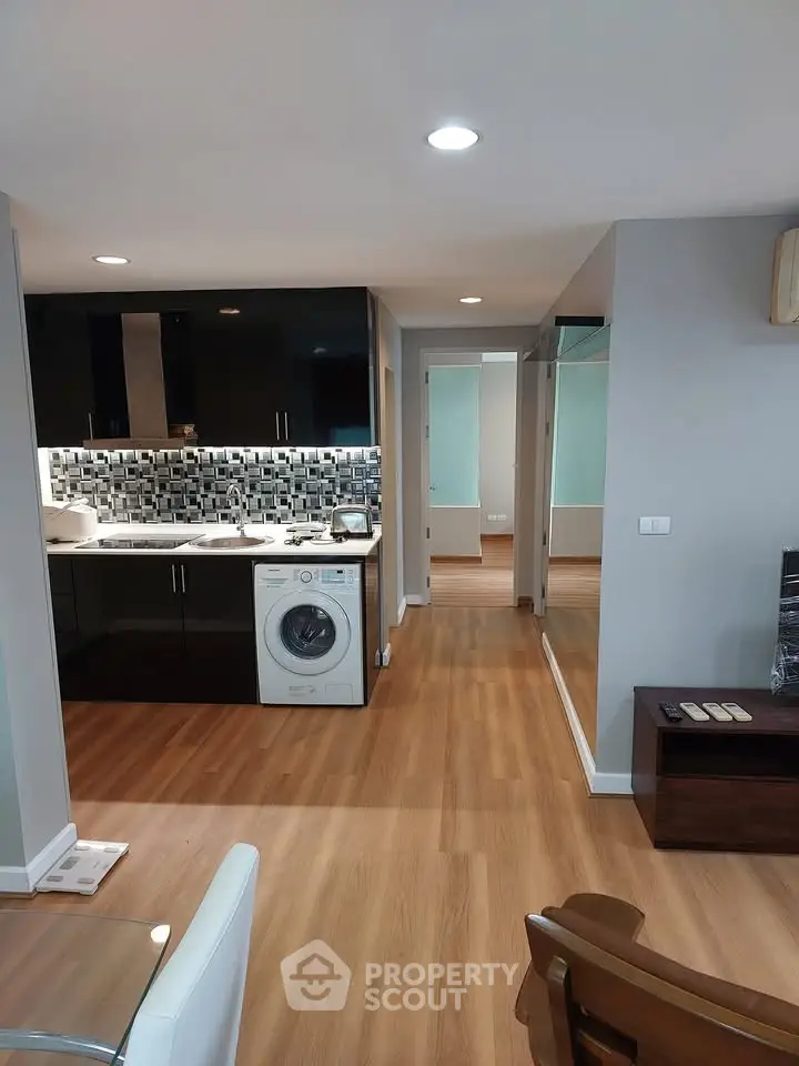 Modern apartment interior with sleek kitchen and washing machine, featuring wood flooring and stylish decor.