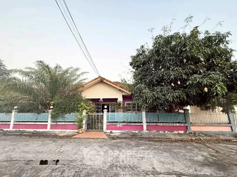 Charming single-story house with colorful fence and lush trees in a serene neighborhood.