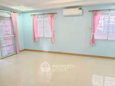 Spacious empty room with pastel blue walls and pink curtains, featuring large windows and air conditioning.