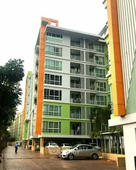 Modern multi-story apartment building with vibrant green and orange accents, featuring covered parking and lush surroundings.