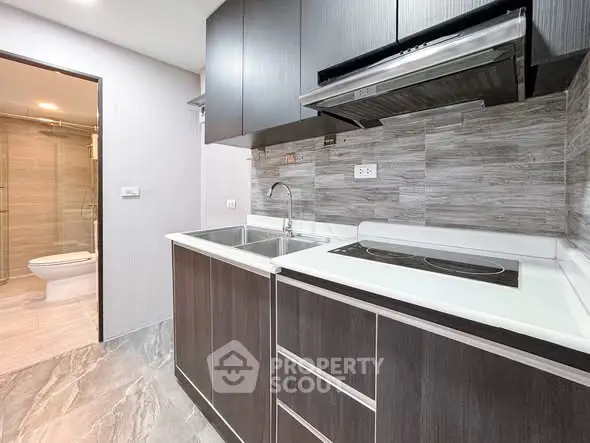 Modern kitchen with sleek cabinetry and electric stove, adjacent to a stylish bathroom.