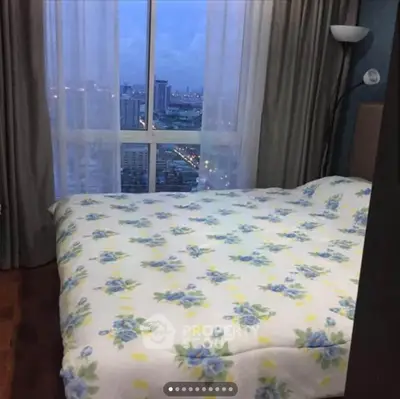 Cozy bedroom with city view, featuring floral bedding and large window for natural light.