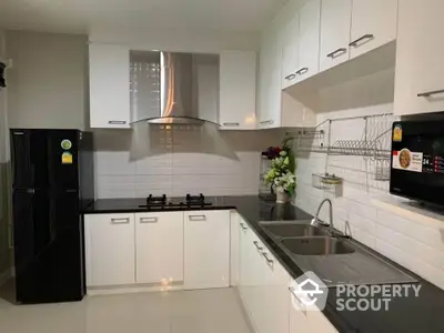 Modern kitchen with sleek black countertops and white cabinets, featuring a gas stove and stainless steel appliances.