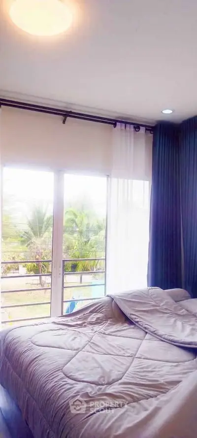 Bright bedroom with large windows and garden view, featuring cozy bedding and elegant curtains.