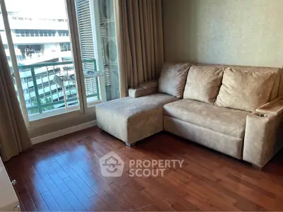 Cozy living room with plush sofa and wooden flooring, featuring a balcony view in a modern apartment.