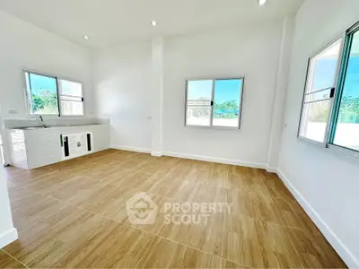 Spacious open-plan living area with large windows and modern kitchen setup, featuring elegant wooden flooring.