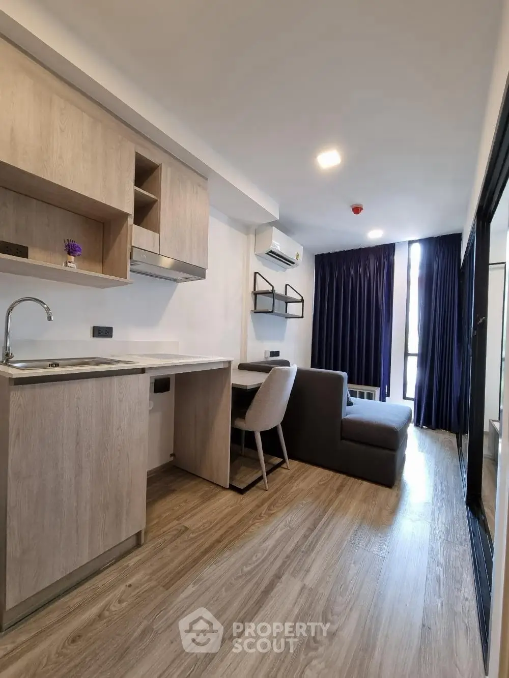 Modern studio apartment with sleek kitchen and cozy living area, featuring wood flooring and ample natural light.