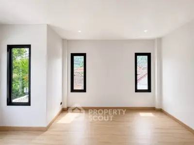Spacious empty room with large windows and wooden flooring, perfect for customization.