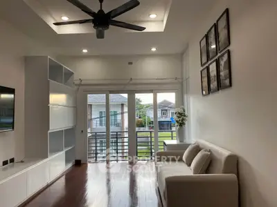 Modern living room with ceiling fan, large windows, and cozy sofa overlooking a suburban view.