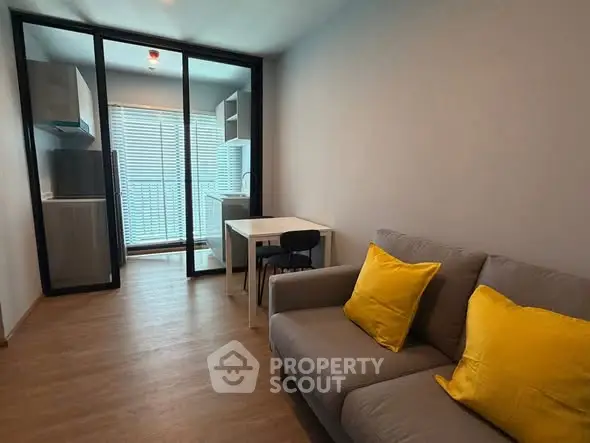 Modern living room with cozy sofa and bright yellow cushions, open layout to kitchen area.