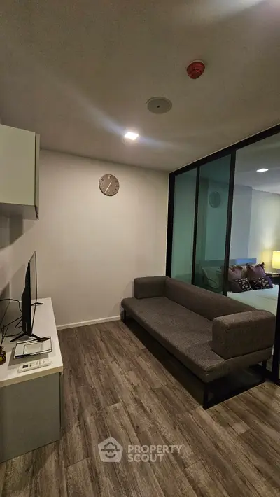 Modern living room with sleek gray sofa and wall-mounted TV, featuring stylish wood flooring.