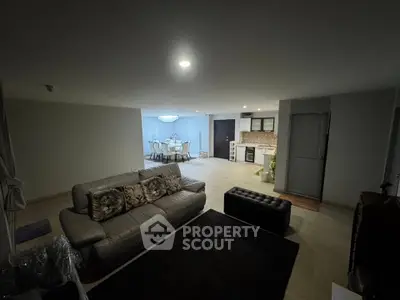 Spacious open-plan living room with modern kitchen and dining area, featuring elegant lighting and cozy seating.