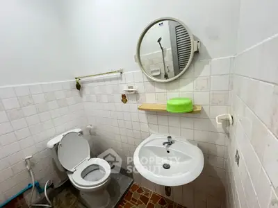 Compact bathroom with white tiles and round mirror, featuring a toilet and sink.