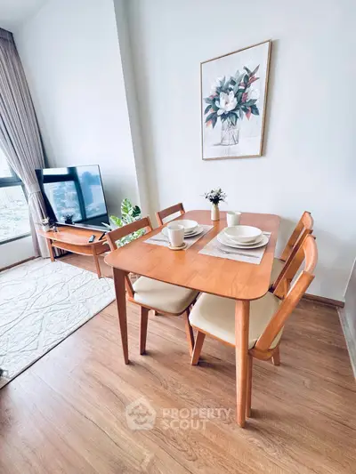 Charming dining area with wooden table and chairs, adjacent to a cozy living room with a TV and large window.