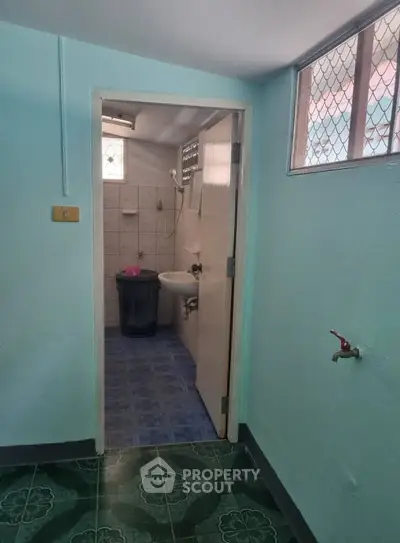 Cozy bathroom with blue tiles and compact layout, featuring a small sink and window for natural light.