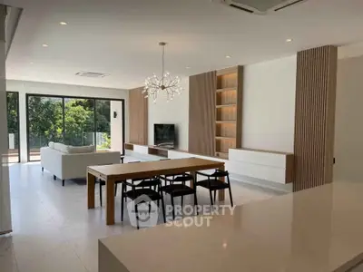 Spacious modern living room with elegant dining area and large windows offering lush green views.
