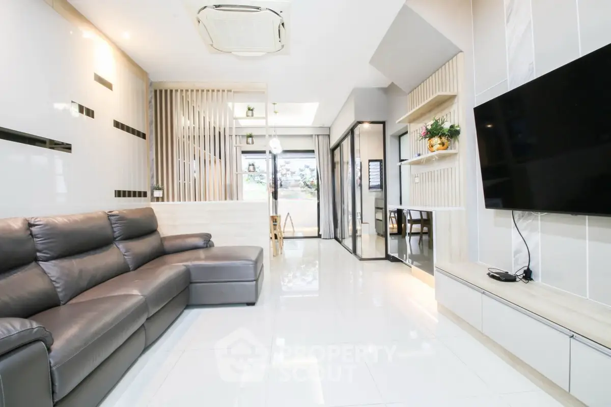 Modern living room with sleek design and large TV, featuring a spacious leather sofa and bright lighting.