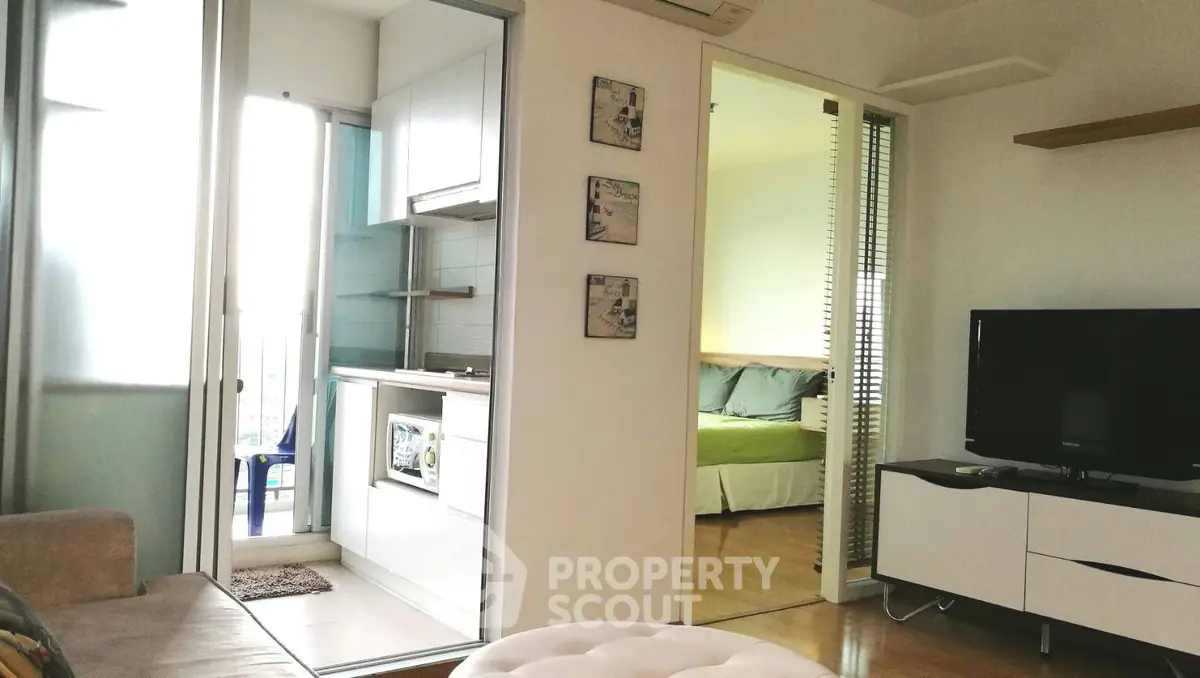 Modern apartment interior with open kitchen and cozy living area, featuring a glimpse of a bedroom.