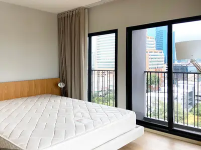 Modern bedroom with large windows and city view, featuring a comfortable mattress and stylish decor.
