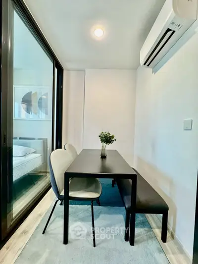 Modern dining area with sleek table and chairs, adjacent to a cozy bedroom, featuring minimalist decor and natural light.