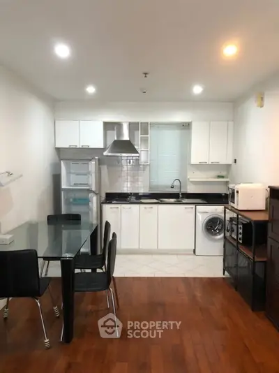 Modern kitchen with dining area, featuring sleek appliances and wooden flooring.