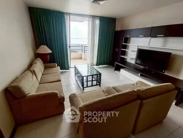 Spacious living room with cozy sofas and a large TV unit, opening to a balcony with natural light.