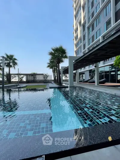 Luxurious poolside view at modern high-rise building with palm trees and clear blue sky.