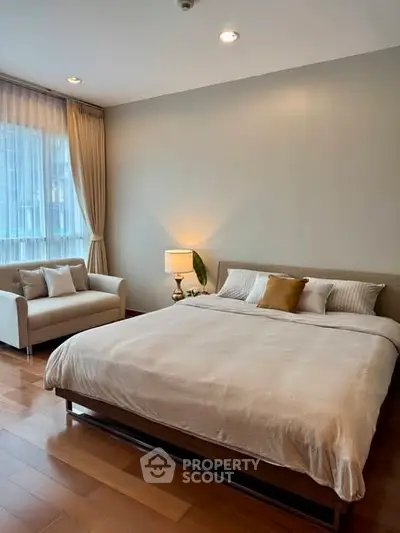 Spacious bedroom with elegant decor and natural light, featuring a cozy sofa and modern lighting.