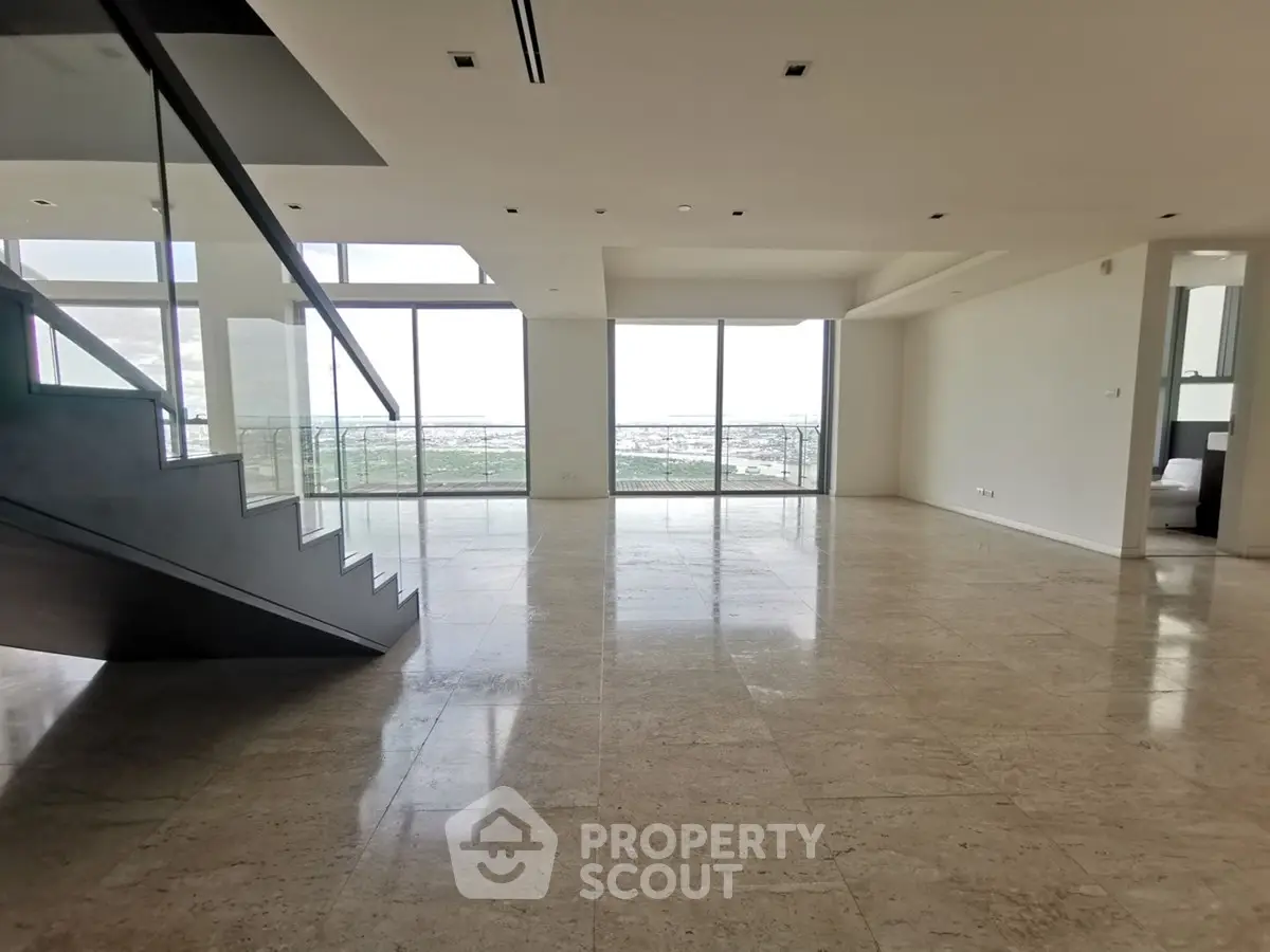 Spacious modern living room with large windows and staircase, offering stunning views and abundant natural light.