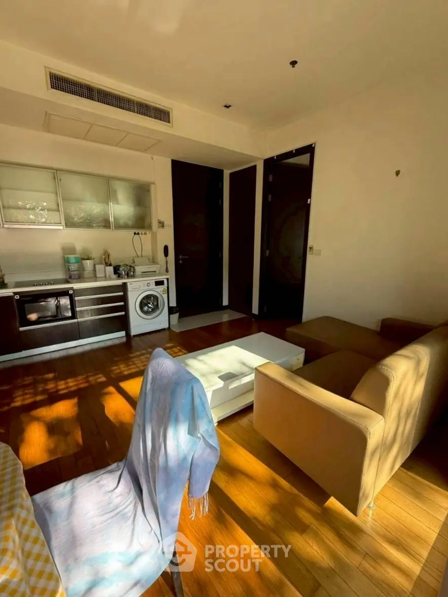 Modern living room with integrated kitchen and washing machine, featuring wooden flooring and cozy seating.