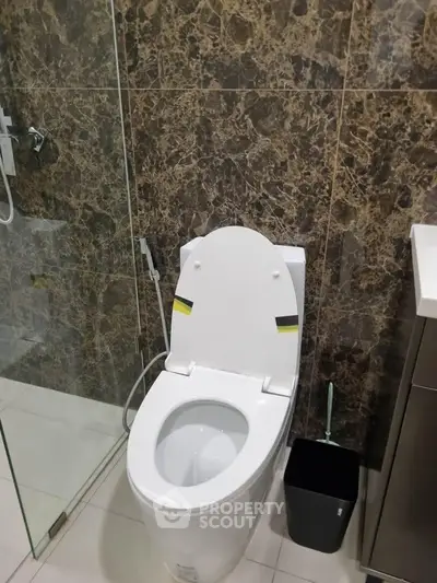 Modern bathroom with sleek toilet and glass shower enclosure, featuring elegant marble wall tiles.