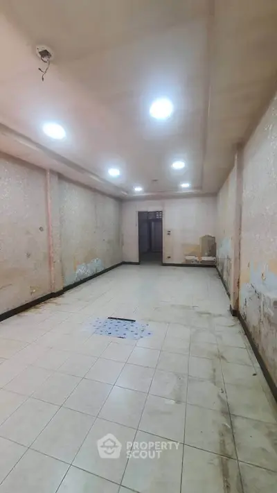 Spacious empty room with tiled flooring and recessed lighting, ideal for renovation.