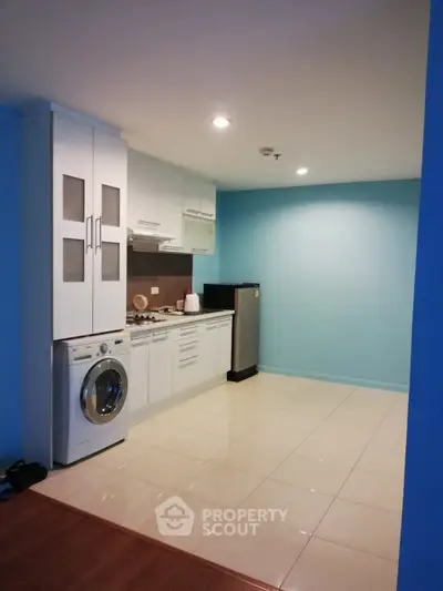 Modern kitchen with washing machine and compact fridge in open layout design.