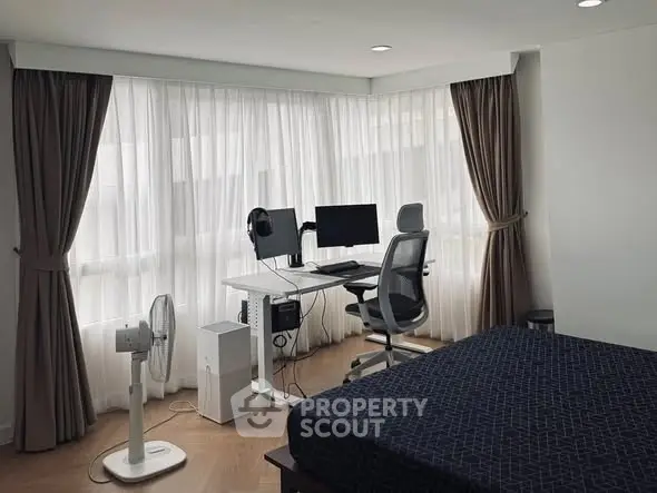 Modern bedroom with study area featuring desk, chair, and dual monitors by large windows.