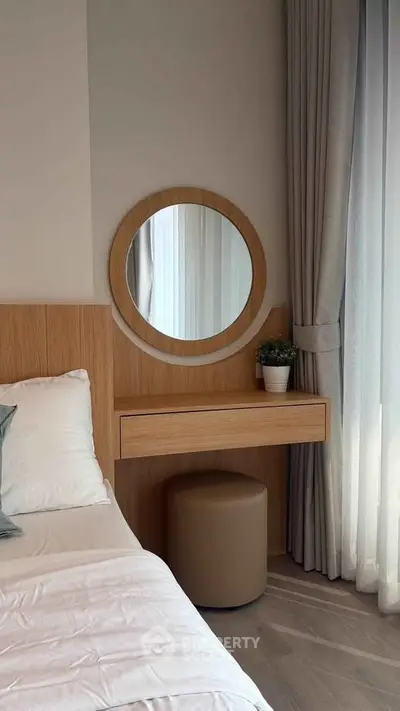 Modern bedroom with stylish wooden vanity and round mirror, featuring elegant curtains and cozy bedding.