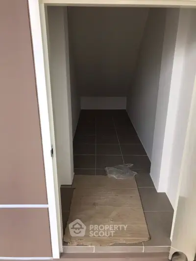Compact storage room with tiled flooring and sloped ceiling, ideal for organizing essentials.