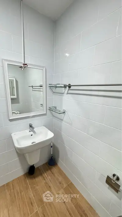 Modern bathroom with sleek white tiles and wooden flooring, featuring a wall-mounted sink and mirror.