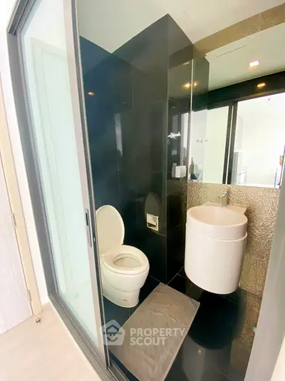 Modern bathroom with sleek black tiles and compact design in a contemporary apartment.