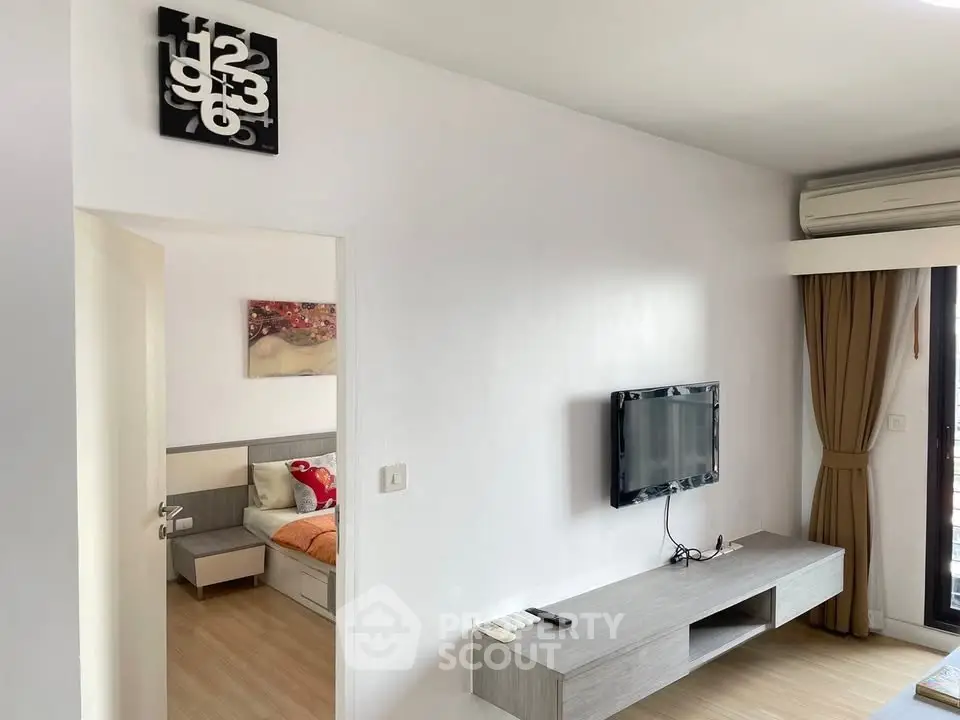 Modern living room with wall-mounted TV and glimpse of cozy bedroom