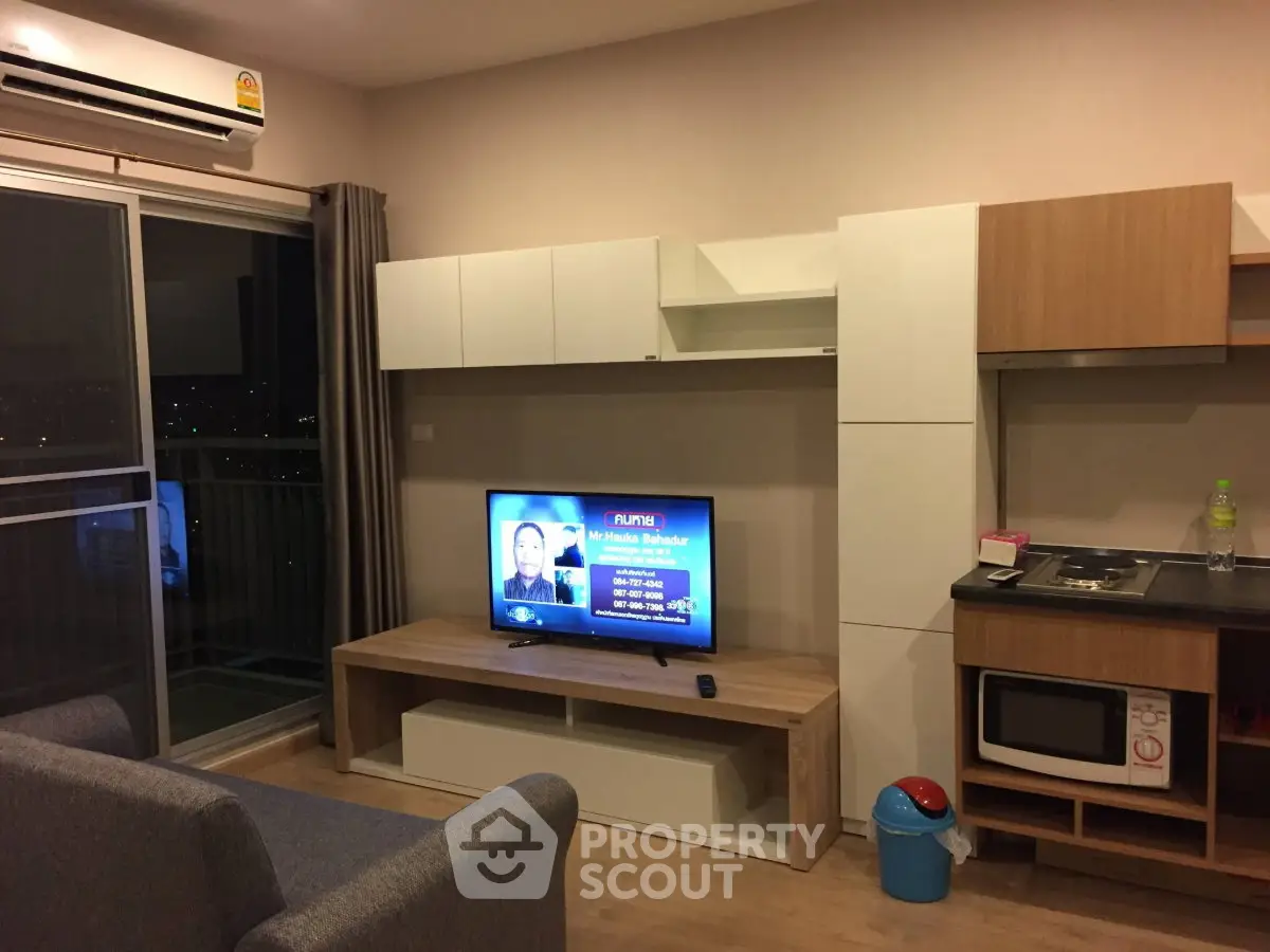 Modern living room with balcony view, sleek furniture, and built-in kitchen appliances.